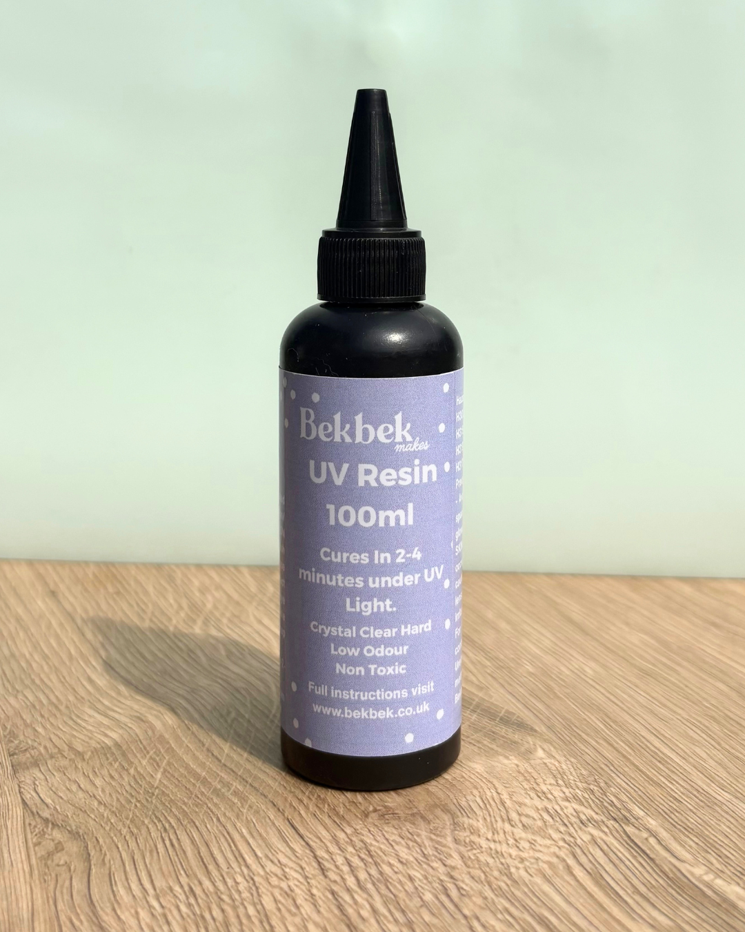 Bottle of Bekbek Makes UV Resin on a wooden surface with a light green background