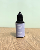 Bottle of Bekbek Makes UV Resin on a wooden surface with a light green background