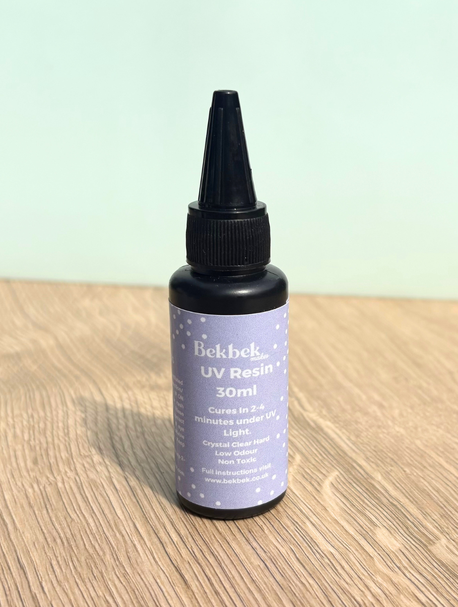 Bottle of Bekbek Makes UV Resin on a wooden surface with a light green background