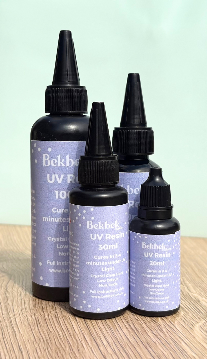 Four bottles of Bekbek Makes UV Resin on a wooden surface with a light green background