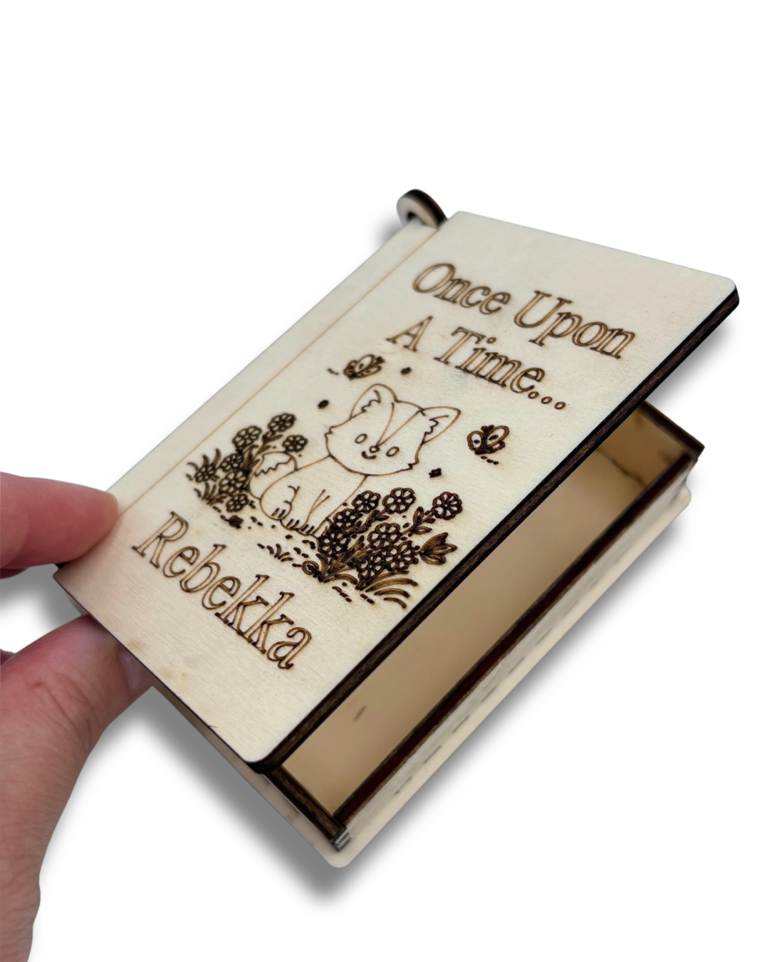 A hand holding a small wooden keepsake box with a laser-engraved cover that reads 'Once Upon A Time.