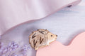 A glittery hedgehog pin badge made of wood, hand-painted and filled with glitter, with a shiny uv resin finish on a pink background.